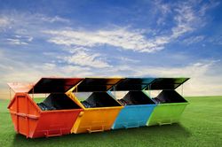Vier bunte Müllcontainer für verschiedene Abfälle stehen auf einer Wiese.