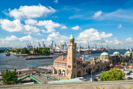 Luftbild Hamburger Hafen mit Speicherstadt, Kränen, Schiffen und historischen Gebäuden bei blauem Himmel.