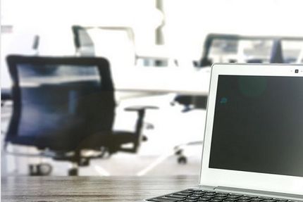 Foto eines Laptops und leerer Bürostühle im HIntergrund