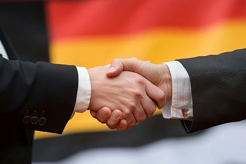 Zwei Geschäftsleute schütteln ihre Hände vor der Deutschland-Flagge.
