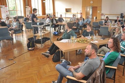 Menschen sitzen in einem Konferenzraum und folgen einer Präsentation