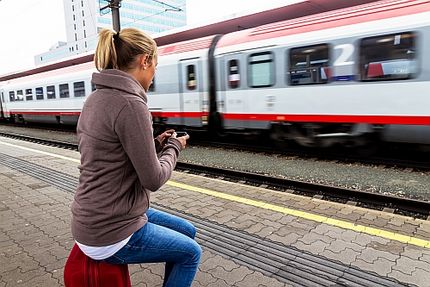 Frau wartet auf Zug und schaut auf Smartphone