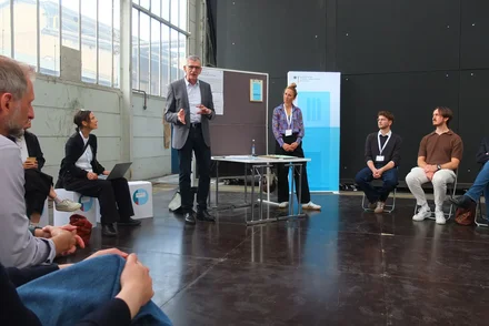 Menschen sitzen in einem Stuhlkreis und hören Bernhard Faller vom vhw zu, der an einer Tafel steht.