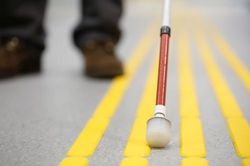 Mensch mit Sehbehinderung läuft mit einem Blindestock auf der Straße