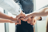 MitarbeiterInnen im Kreis stoßen ihre Fäuste in der Mitte zusammen.