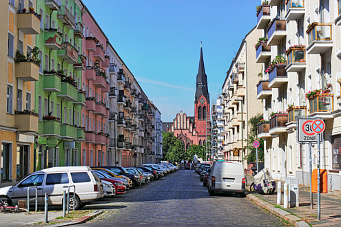 Foto einer Straße im Erhaltungsgebiet Berlin-Friedrichshain gesäumt von Altbauten und mit Kirche am Straßenende