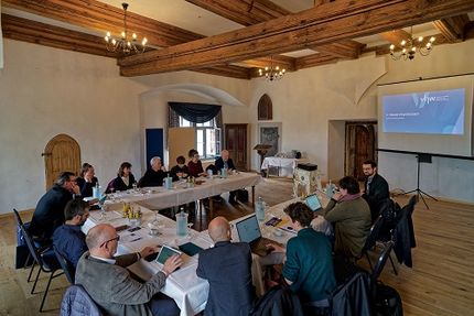 Teilnehmende der Abschlussveranstaltung sitzen an Tischen und diskutieren.