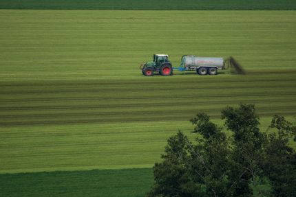 Foto eines Traktor, der mit einem Güllewagen Gülle auf ein Feld ausbringt.