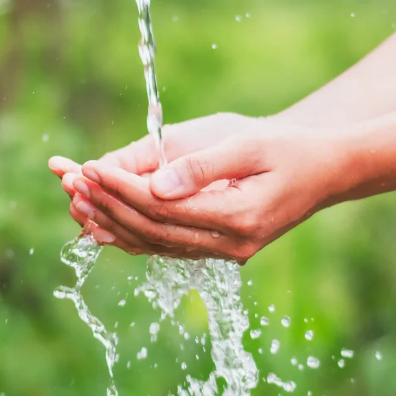 Eine Person hält die Hände unter einem Strahl frischen Wassers und sammelt es in den Händen.