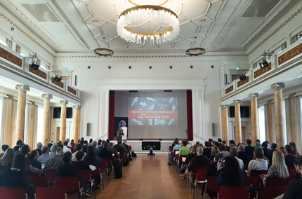 Der festliche Veranstaltungssaal in der Leopolidina in Halle anlässlich des ARL-Kongresses. Der Blick ist vom Mittelgang am hinteren Ende auf die Eröffnungspräsentation gerichtet, die Sitzreihen sind gut gefüllt. 