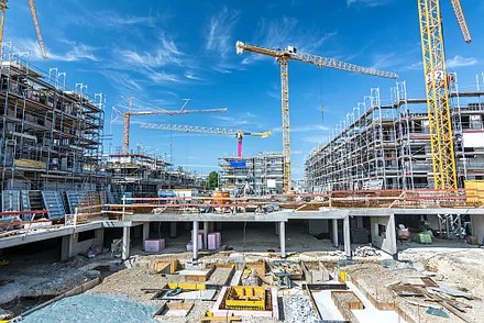 Eine großflächige Baustelle mit Baukränen, Maschinen und Arbeiten im urbanen Umfeld.