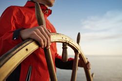 Foto: Skipper auf See hält großen Segelbootsteur in der Hand.