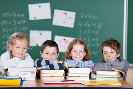 Foto von Grundschulkindern im Klassenraum an einem Tisch mit Büchern, im Hintergrund eine Schultafel.