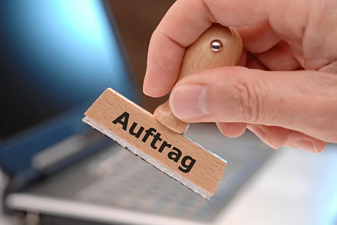 Auftragsvergabe im geschäftlichen Kontext Eine Person hält einen Stempel mit der Aufschrift „Auftrag“ in der Hand.