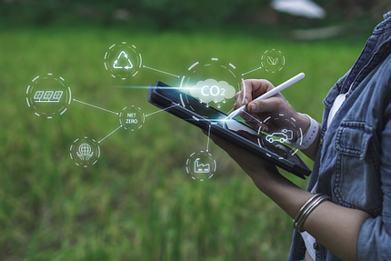 Frau in der Natur hält Stift auf Tablet. Eingeblendete Icons symbolisieren Maßnahmen zur CO2-Reduzierung, z.B. durch Einsatz regenerativer Energien 