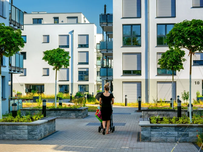 Mietrecht und Wohnungswirtschaft Frau mit Kinderwagen im begrünten Innenhof einer modernen Wohnanlage mit weißen Mehrfamilienhäusern