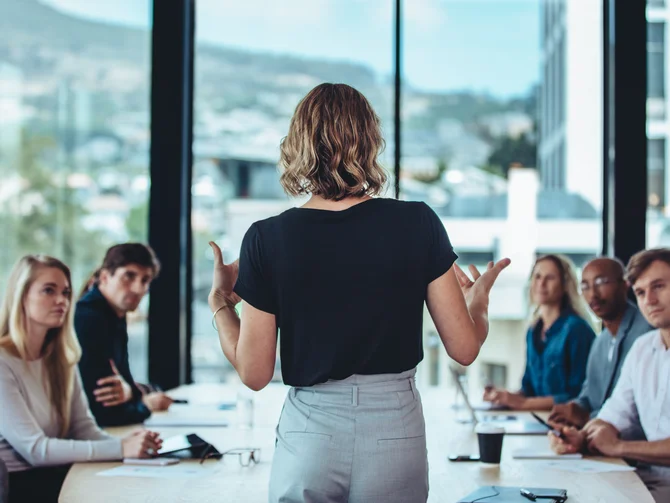 fuehrung-personalentwicklung-c-jacoblund-adobestock Referentin von hinten gestikulierend vor fünf konzentrierten Teilnehmenden an einem Konferenztisch