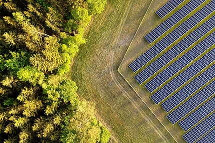 Luftbild einer Freiflächen-Photovoltaikanlage am Waldrand.