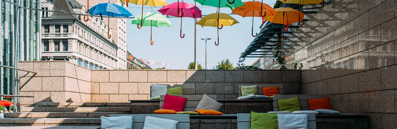 Bunte Regenschirme über urbaner Treppensituation mit Sitzkissen in Großsiedlung.