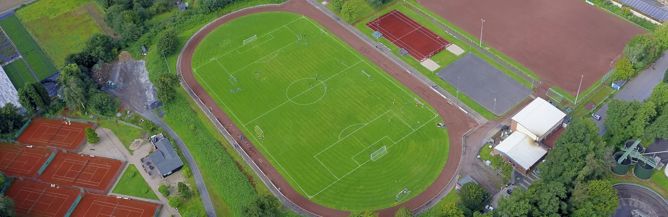 Luftbild einer Sportanlage mit Fußballplatz, Tennisplätzen, Laufbahn und umgebenden Grünflächen in ländlichem Raum.