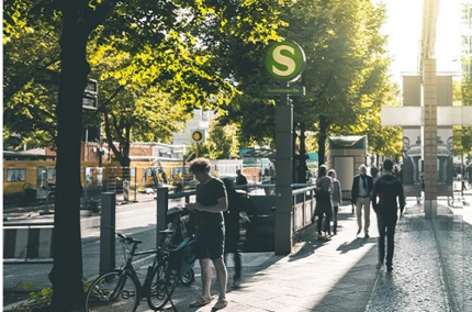 Straßenszene mit S-Bahnhof, Menschen zu Fuß und mit dem Fahrrad