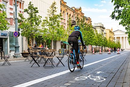 Fahrradfahrer fährt auf Fahrradweg durch verkehrsberuhigte Straße mit Außensitzen