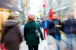 Stadtplanung für Einzelhandel und Versorgung: Viele Menschen laufen schnell durch eine Innenstadt mit Einzelhandelsgebäuden.
