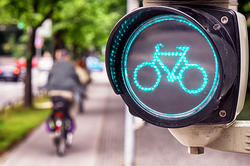 Foto einer grünen Fahrradampel am Radweg mit Radfahrern.