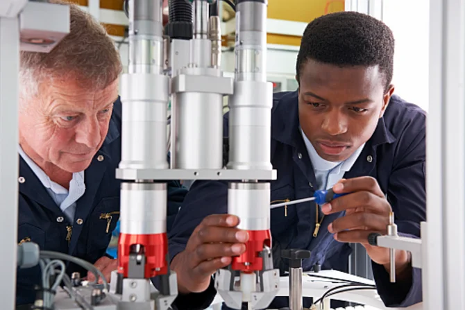 Integration in der Ausbildung Zwei Personen: Ein Ausbilder und ein Lehrling mit Migrationshintergrund arbeiten an einer Maschine.