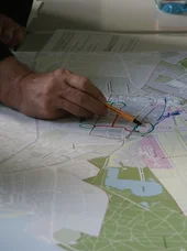 Zertifikatslehrgang Moderator SE Die Abbildung zeigt Menschen, die eine große Übersichtskarte analysieren, was zur Planung von Routen oder zur Orientierung im Gelände genutzt wird.