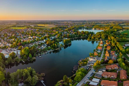 Panoramaluftbild einer norddeutschen Kleinstadt mit See, Wohnbebauung und Windrädern im Abendlicht