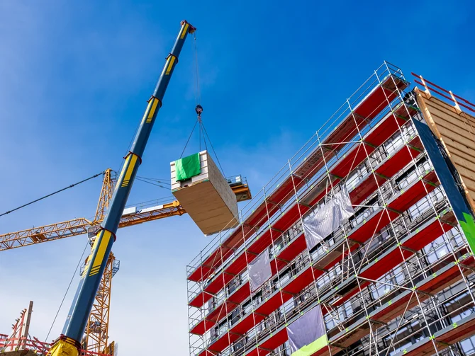 Öffentliches Immobilienmanagement Froschperspektive auf Baustelle mit Kran, Holzbauelement und eingerüstetem Mehrgeschossbau vor blauem Himmel