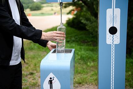 Foto: Mann für seine Wasserflasche an einem Wasserspender-Automat in der Stadt.the city. Free public water bottle refill station. Sustainable and green city. Male in black coat. Tap water to reduce plastic bottle usage. Drinking water dispenser