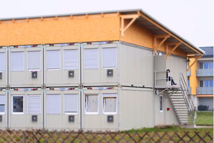 Symbolbild einer Container-Flüchtlingsunterkunft vor einem Wohnhaus 