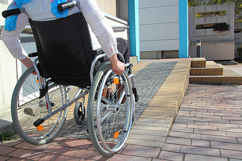 Rollstuhlfahrerin auf Rollstuhlrampe eines öffentlichen Gebäudes