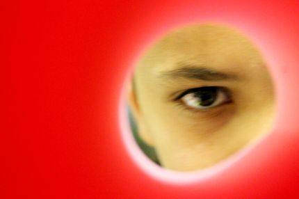 Foto eines Menschen, der durch ein Loch in einer roten Wand blickt