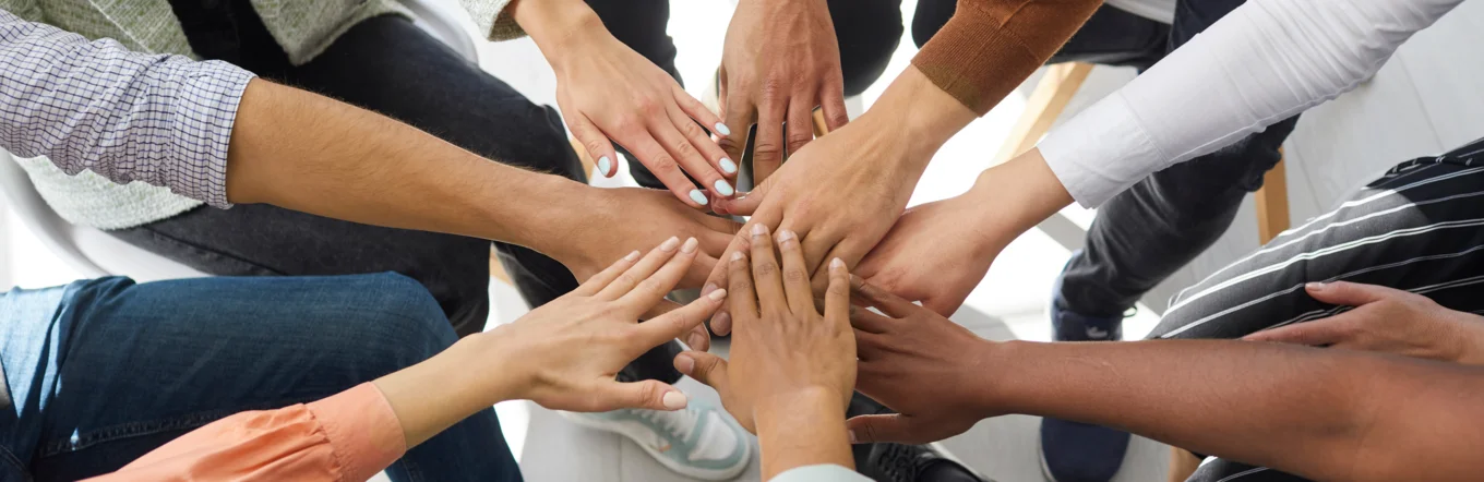 Gruppe junger Menschen legt Hände aufeinander als Zeichen von Teamgeist und Gemeinschaft