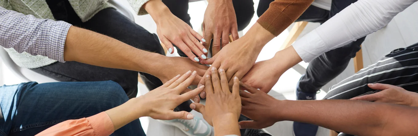 Gruppe junger Menschen legt Hände aufeinander als Zeichen von Teamgeist und Gemeinschaft