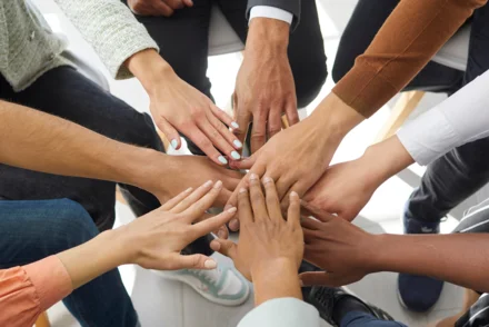 Gruppe junger Menschen legt Hände aufeinander als Zeichen von Teamgeist und Gemeinschaft