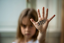 Foto: Mädchen streckt eine mit "Stop" beschriebene Hand nach vorne aus. 