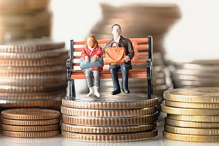 Kleine Figuren sitzen auf einer Bank, die auf 50-Cent-Münzen steht. Drumherum sind weitere Münzen zu erkennen.