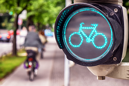 Foto von einer grüne Fahrradampel am Radweg, mit Radfahrern im Hintergrund.