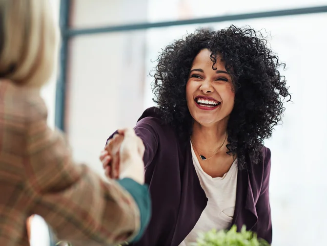 personalrecht-c-daniel-laflor-peopleimages.com Zwei Frauen beim Händeschütteln – lachende Bewerberin im lila Blazer im Vorstellungsgespräch