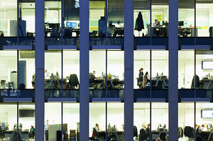 Fassade eines Bürohauses mit erleuchteten Fenster, durch die Büros mit arbeitenden Menschen zu sehen sind.
