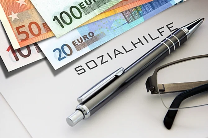 Sozialhilfe und finanzielle Unterstützung Oben im Bild liegen mehrere Geldscheine. Darunter ist die Beschriftung „Sozialhilfe“ zu erkennen. Unter „Sozialhilfe“ befinden sich ein Kugelschreiber und eine Brille.