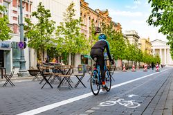 Straße mit Gastronomiestühlen und -tischen, Fahrradfahrer auf Fahrradweg