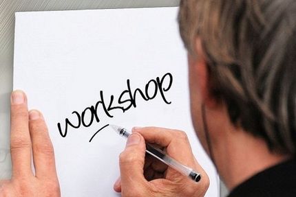 Ein Mensch schreibt mit einem schwarzen Stift das Wort "Workshop" auf einen Zettel.