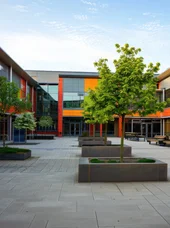 Dieses Bild zeigt Schulhof und modernes Schulgebäude mit bunten Fassadenelementen.
