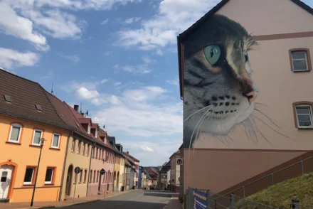 Kleinstädtischer Straßenzug mit bunten Reihenhäusern und großformatigem Katzen-Wandgemälde an Hausgiebel