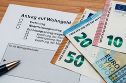 Foto: Kugelschreiber und Geldscheine liegen auf einem Antrag auf Wohngeld.